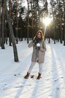 una joven y alegre chica caucásica con un abrigo marrón sostiene una bola de nieve en un bosque cubierto de nieve en invierno. foto de ojo de pez