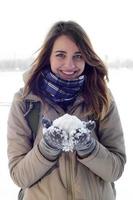 una joven y alegre chica caucásica con un abrigo marrón sostiene una bola de nieve en el fondo de una línea de horizonte entre el cielo y un lago congelado en invierno foto