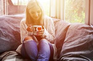 Blonde girl in a warm sweater with a cup of coffee sitting on a photo
