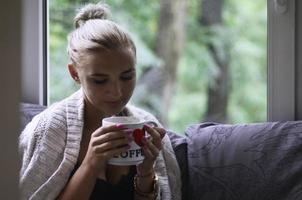 Blonde girl in a warm sweater with a cup of coffee sitting on a photo