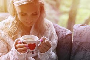 Blonde girl in a warm sweater with a cup of coffee sitting on a photo