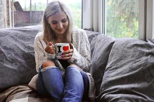 Blonde girl in a warm sweater with a cup of coffee sitting on a photo