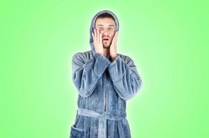 Portrait of young caucasian bearded man in blue bathrobe be scared isolated on green background photo
