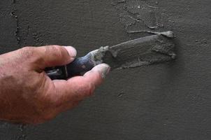 Hands of an old manual worker with wall plastering tools renovating house. Plasterer renovating outdoor walls and corners with spatula and plaster. Wall insulation. Construction finishing works photo