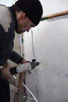 An elderly workman drills a hole in a styrofoam wall for the subsequent installation of a plastic reinforcing dowel. Creating holes in the wall with a drill. Warming of the building facade photo