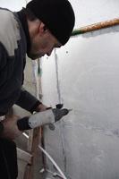 un trabajador anciano perfora un agujero en una pared de espuma de poliestireno para la posterior instalación de una espiga de refuerzo de plástico. creando agujeros en la pared con un taladro. calentamiento de la fachada del edificio foto