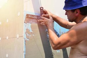 Fifty years old manual worker with wall plastering tools renovating house. Plasterer renovating walls and corners with spatula and plaster. Wall mash installation. Construction finishing works photo