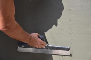 Hands of an old manual worker with wall plastering tools renovating house. Plasterer renovating outdoor walls and corners with spatula and plaster. Wall insulation. Construction finishing works photo