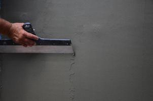 Hands of an old manual worker with wall plastering tools renovating house. Plasterer renovating outdoor walls and corners with spatula and plaster. Wall insulation. Construction finishing works photo