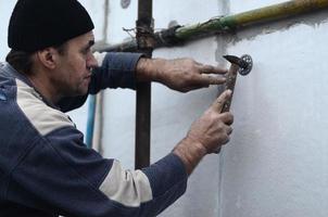 An elderly workman clogs a dowel into a plastic umbrella mount in a styrofoam wall. The process of fixing expanded polystyrene plates. Warming of the facade of the building photo