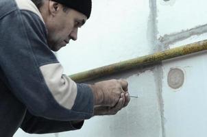 An elderly worker creates holes in the expanded polystyrene wall for the subsequent drilling and installation of an umbrella dowel. The process of fixing expanded polystyrene plates. Insulation work photo
