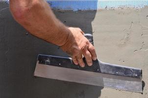 Hands of an old manual worker with wall plastering tools renovating house. Plasterer renovating outdoor walls and corners with spatula and plaster. Wall insulation. Construction finishing works photo