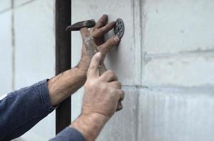 un trabajador anciano obstruye una espiga en un paraguas de plástico montado en una pared de espuma de poliestireno. el proceso de fijación de placas de poliestireno expandido. calentamiento de la fachada del edificio foto