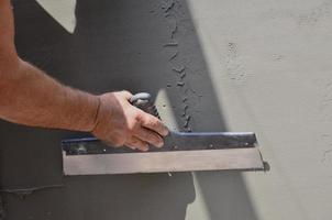 Hands of an old manual worker with wall plastering tools renovating house. Plasterer renovating outdoor walls and corners with spatula and plaster. Wall insulation. Construction finishing works photo