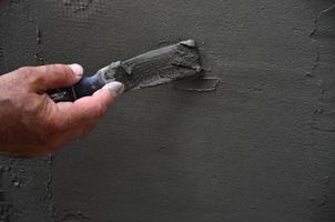 Hands of an old manual worker with wall plastering tools renovating house. Plasterer renovating outdoor walls and corners with spatula and plaster. Wall insulation. Construction finishing works photo