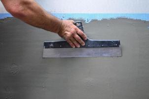 Hands of an old manual worker with wall plastering tools renovating house. Plasterer renovating outdoor walls and corners with spatula and plaster. Wall insulation. Construction finishing works photo