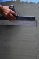 Hands of an old manual worker with wall plastering tools renovating house. Plasterer renovating outdoor walls and corners with spatula and plaster. Wall insulation. Construction finishing works photo