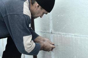 un trabajador de edad avanzada crea agujeros en la pared de poliestireno expandido para la posterior perforación e instalación de una clavija de paraguas. el proceso de fijación de placas de poliestireno expandido. trabajo de aislamiento foto