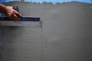 Hands of an old manual worker with wall plastering tools renovating house. Plasterer renovating outdoor walls and corners with spatula and plaster. Wall insulation. Construction finishing works photo