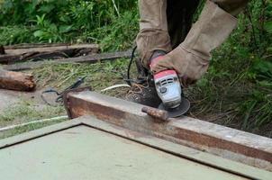 Electric wheel grinding on steel structure outdoors. Old manual worker in protective gloves cutting metal door with grinder photo