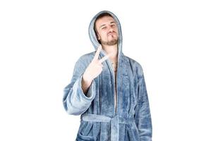 Portrait of young caucasian bearded man in blue bathrobe shows victory or peace gesture isolated on white background photo