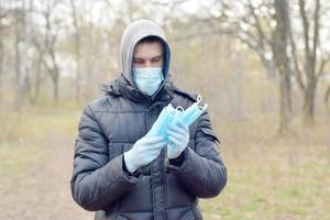 Young man in protective mask shows bunch of protective face masks outdoors in spring wood photo
