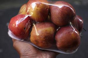 black skin with six apples wrapped in transparent plastic isolated on brown background holding one hand. photo