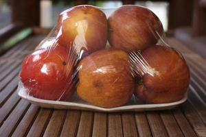 black peel with six apples wrapped in transparent plastic isolated on brown background photo