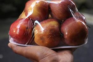 black skin with six apples wrapped in transparent plastic isolated on brown background holding one hand. photo