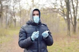 Young man in protective mask shows sanitizer spray bottles outdoors in spring wood photo