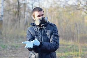 Portrait of young man in protective gas mask wears rubber disposable gloves outdoors in spring wood photo