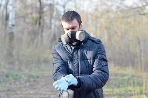 Portrait of young man in protective gas mask wears rubber disposable gloves outdoors in spring wood photo