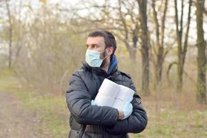 Covidiot concept. Young man in protective mask holds many rolls of toilet paper outdoors in spring wood photo