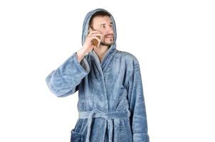 Portrait of young caucasian bearded man in blue bathrobe talks on smartphone isolated on white background photo