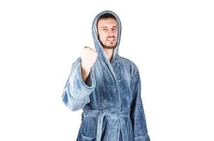 Portrait of young caucasian bearded man in blue bathrobe raises fist isolated on white background photo