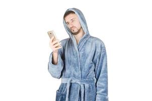 retrato de un joven caucásico con barba y albornoz azul mirando a la pantalla del smartphone aislado de fondo blanco foto