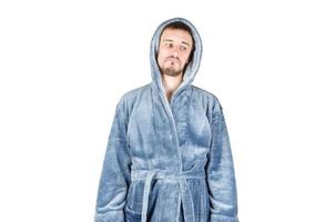 Portrait of young caucasian bearded man in blue bathrobe shows sad emotion on white background photo