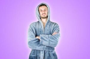 Portrait of young caucasian bearded man in blue bathrobe with crossed hands isolated on purple background photo
