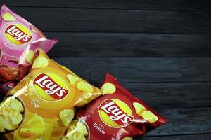 KHARKOV, UKRAINE - JANUARY 3, 2021 Various flavoured of lay's potato chips on wooden background. Lay's has been owned by PepsiCo through Frito-Lay in 1965 photo
