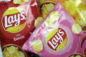 KHARKOV, UKRAINE - JANUARY 3, 2021 Various flavoured of lay's potato chips on wooden background. Lay's has been owned by PepsiCo through Frito-Lay in 1965 photo