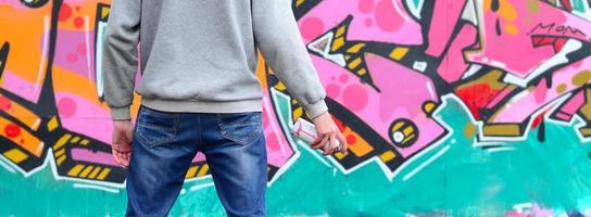 A young graffiti artist in a gray hoodie looks at the wall with photo