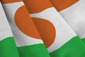 Niger flag with big folds waving close up under the studio light indoors. The official symbols and colors in banner photo