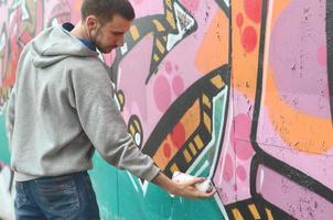 un joven con una sudadera con capucha gris pinta graffiti en rosa y verde c foto