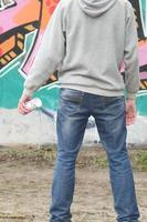 A young graffiti artist in a gray hoodie looks at the wall with photo