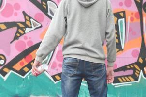 A young graffiti artist in a gray hoodie looks at the wall with photo