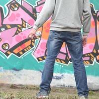 un joven grafitero con una capucha gris mira la pared con foto