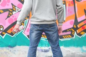 A young graffiti artist in a gray hoodie looks at the wall with photo