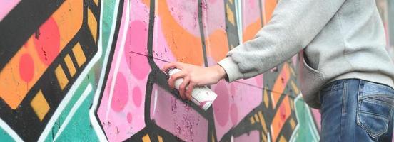 la mano de un joven con una capucha gris pinta graffiti en rosa y foto