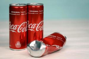 KHARKOV, UKRAINE - DECEMBER 8, 2020 Coca Cola aluminium drink cans on white table. Coca Cola or Coke is a carbonated soft drink manufactured by The Coca-Cola Company photo