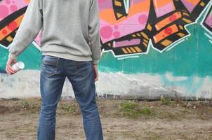 A young graffiti artist in a gray hoodie looks at the wall with photo